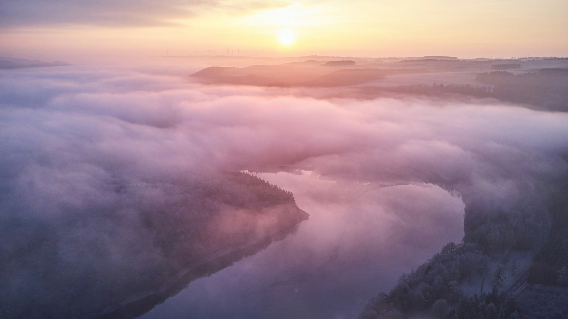 Mist drifting over a valley at dawn, the sun rising through pink and lavender fog